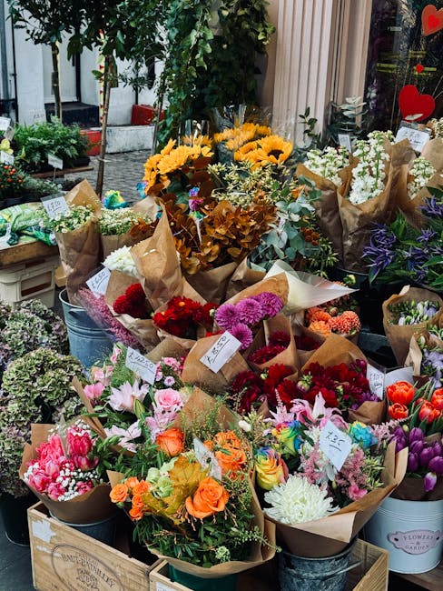 An outdoor display of freshly arranged flower bouquets featuring a vibrant mix of flowers including sunflowers with bright yellow petals, pink lilies with delicate petals, deep red roses, purple irise